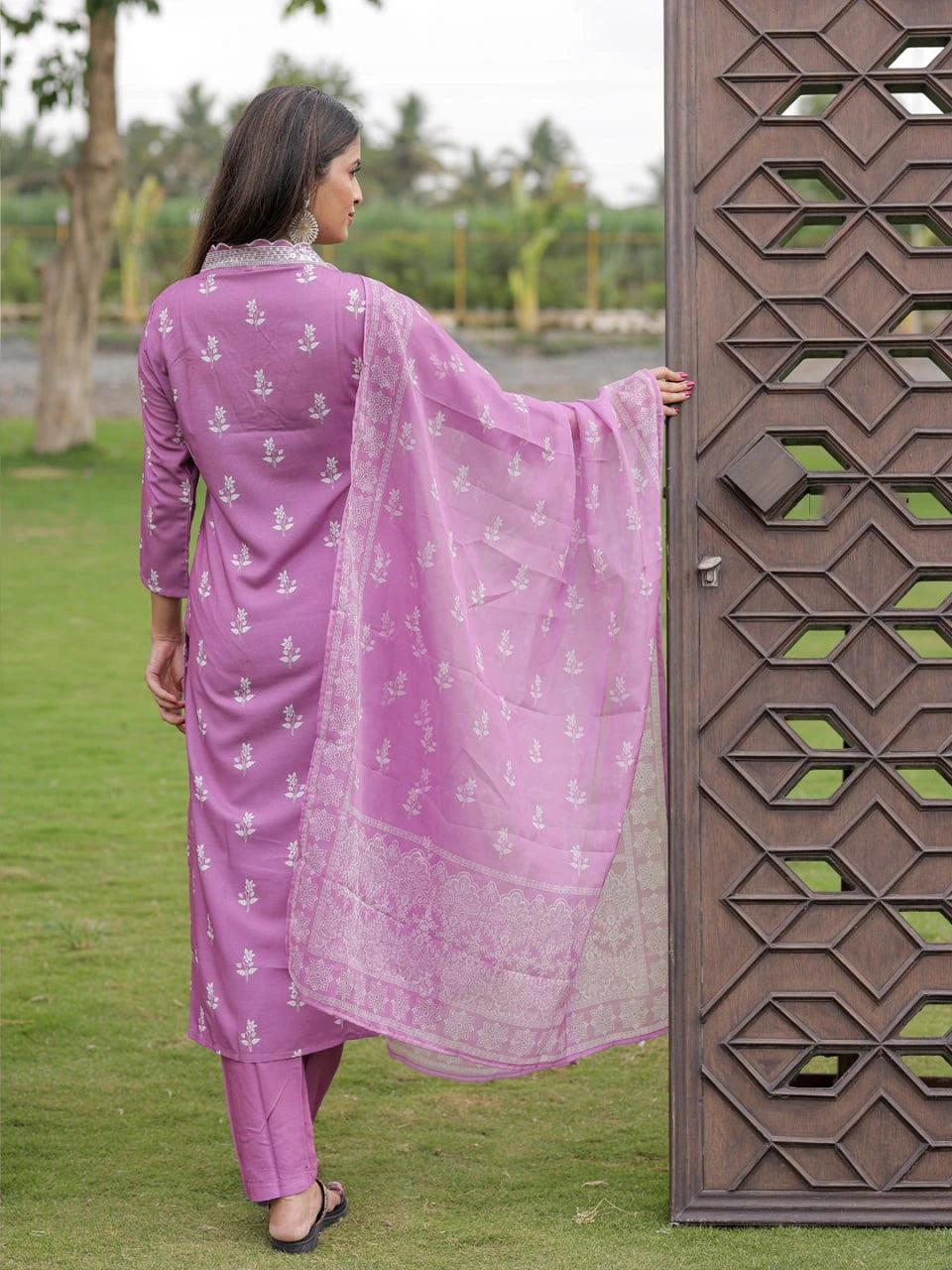 Woman in a pink traditional outfit standing next to a decorative metal gate outdoors.
